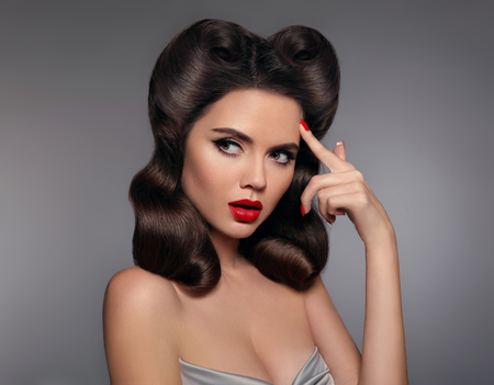 Pin up girl with red lips makeup and retro curls hair style. Retro woman looking to the side holds a...