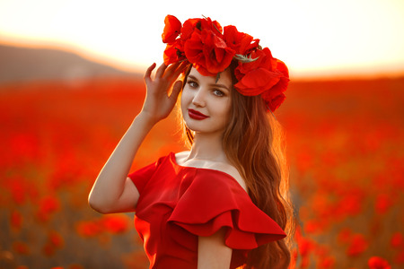 Beautiful girl in red poppy field at sunset. Free Happy Woman Enjoying Nature. Beauty female Outdoor portrait. Freedom concept. Enjoyment.の写真素材