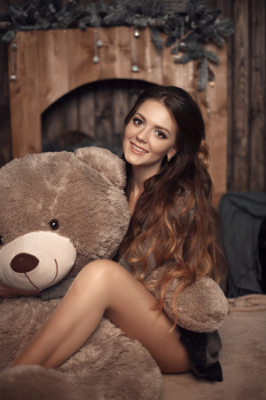 Pretty cute brunette girl posing with big teddy bear on the floor in cozy comfortable interior home.の写真素材