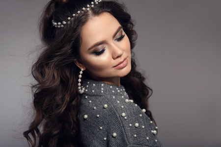 Beautiful brunette portrait. Pearls jewelry women set. Beauty makeup. Curly long hair style. Gorgeous girl model with matte lipstick isolated on studio gray background.の写真素材