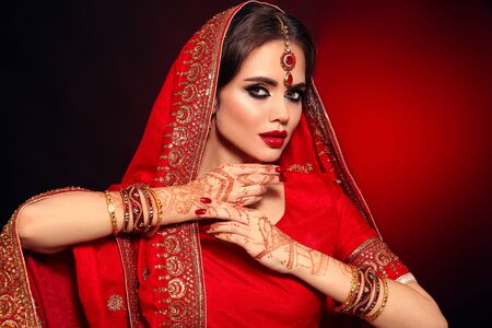 Portrait of beautiful indian girl in red bridal sari. Young hindu woman model with kundan jewelry set. Traditional Indian costume lehenga choli. Henna painting, mehendi on bride's hands.の写真素材