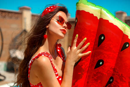 Beautiful woman in Vintage polka dots swimsuit with watermelon lilo float mattress by swimming pool...