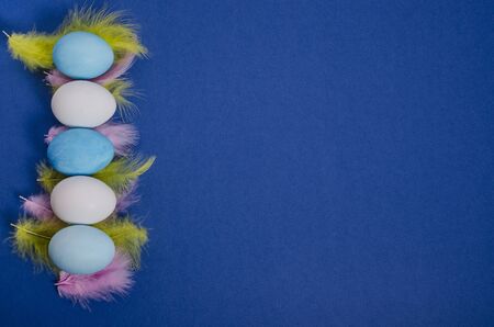 White and blue easter eggs with feathers on a classic blue background with copy space. View from...