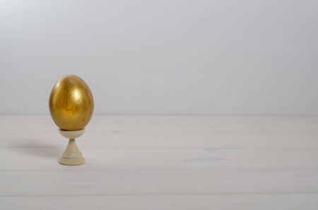 Easter card background. Easter golden egg on a white wooden background with copy space. Happy...