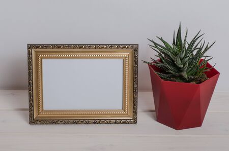 Mock up frame on a white wooden table with cactus in the room. Desktop.