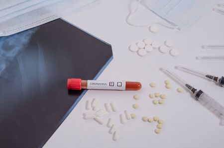 Positive blood test for coronavirus, lung x-ray, surgical medical mask and medication on a white...