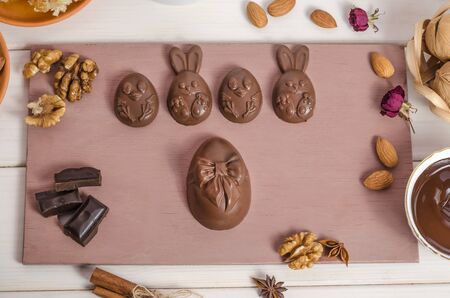 Home made chocolate easter eggs in the shape of a rabbit and chicken on a wooden white background with melted chocolate and nuts. Preparing for Easter. Happy easter.の写真素材
