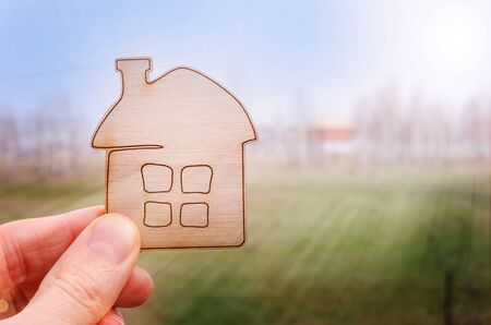 A model of a house in the hand of a real estate agent or a person who dreams of buying his house on the background of the sky and a meadow with a copy space. Home purchase offer, property insurance, affordable housing concept.の写真素材