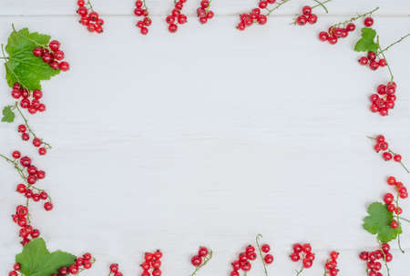 Frame of red currant berries on a white wooden background with copy space. For summer lettering.