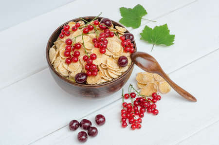 Fresh cornflakes with currants and cherries in a round bowl on a white wooden background.の写真素材