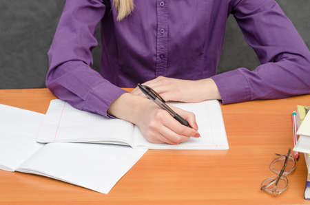 Girl student sits at a table and writes an abstract. School lessons, classes at the university.