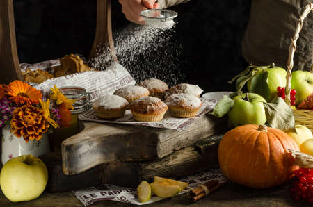 Woman sprinkle icing sugar on delicious homemade apple and pumpkin muffins on dark background, halloween bakingの写真素材