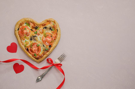 Pizza in the form of a heart on a beige background with red hearts with a fork with a red ribbon. Order pizza for a romantic dinner on Valentine's Day. Love.の写真素材