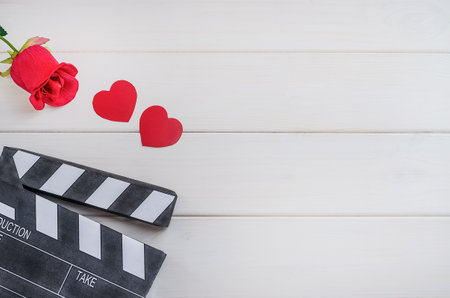 Cinema on Valentine's Day. Movie advertisement. Cinema clapper board with hearts and a rose on a white wooden background. Romantic movie.の写真素材
