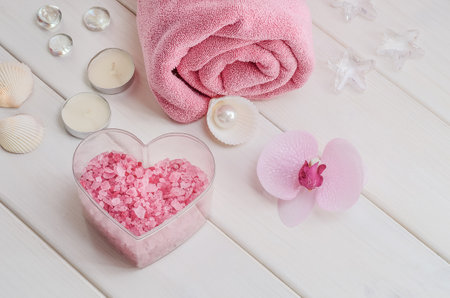Spa treatments as a gift for Valentine's Day. Pink towel with flower, shells and pink sea salt in the shape of a heart on a white wooden background. Beauty salon, massage.の写真素材