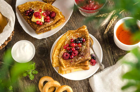 Pancakes with berries with tea, sour cream for the Russian holiday Maslenitsa on a wooden background...