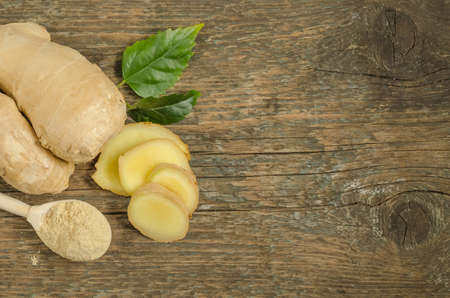 Ginger root with chopped wedges and dry powder on wooden background with copy space