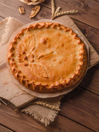 Delicious fresh round pie stuffed with curly dough decorations on wooden backgroundの写真素材