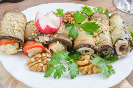 Healthy eggplant rolls stuffed with cheese, served with vegetables and herbs close-up on a white plate on a dark wooden backgroundの写真素材