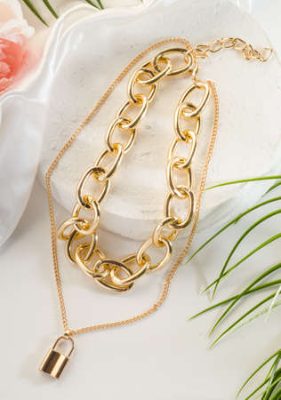 Fashion bijouterie - double gold chain with a lock on a white stand, close up