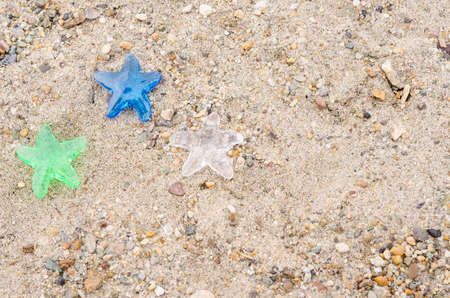 Three decorative stars on a background of beach sand with a copy space, the concept of a holiday in...