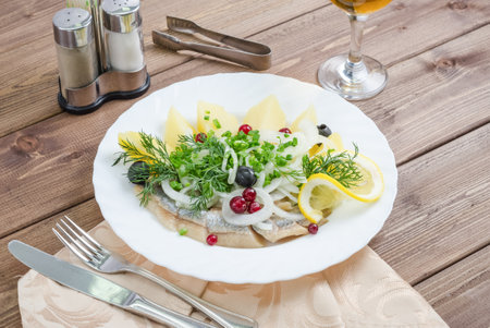 Herring with potatoes, onions and dill on a white plate on a dark wooden backgroundの写真素材