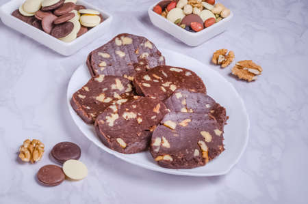 Dessert chocolate sausage with nuts on a white plate on a marble backgroundの写真素材