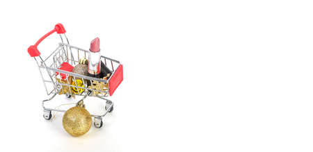 Concept of christmas sales of cosmetics, lipstick and christmas toys in a trolley on a white background, banner with copy spaceの写真素材