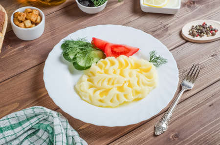 Delicious mashed potatoes with butter, fresh vegetables on a white plate on a dark wooden backgroundの写真素材
