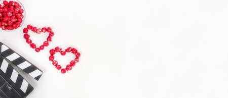 Valentine's Day movie concept. Clapperboard with hearts made of red caramel popcorn with copy space on a white background.の写真素材