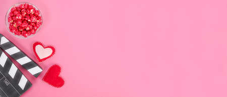 Valentine's Day movie concept. Movie clapperboard with hearts and red caramel popcorn with copy space on pink background.の写真素材