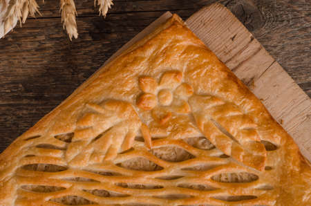 Delicious fresh square pie stuffed with curly dough decorations close-up on wooden background