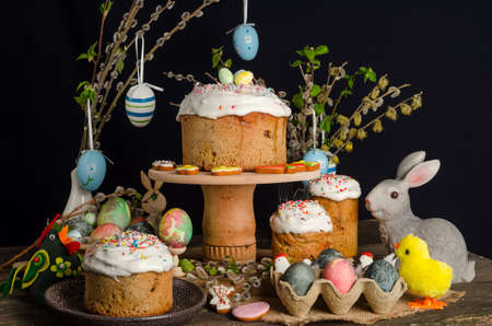 Easter cakes and eggs on a festive Easter table with willow and a figurine of a rabbit on a dark...