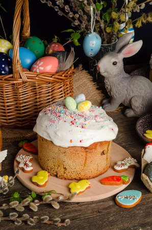 Easter cake and eggs on a festive Easter table with willow and a figurine of a rabbit on a dark background.の写真素材