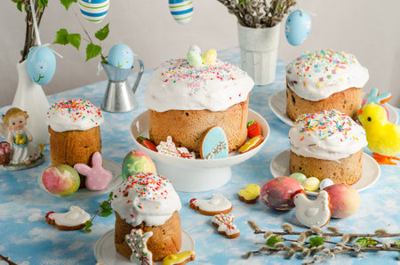 Easter cakes and eggs on a festive Easter table with willow and a figurine of a rabbit on a blue...