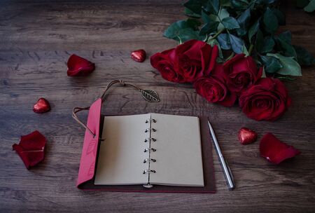 notebook for writing with a pen and bouquet of red fragrant roses on a wooden backgroundの写真素材