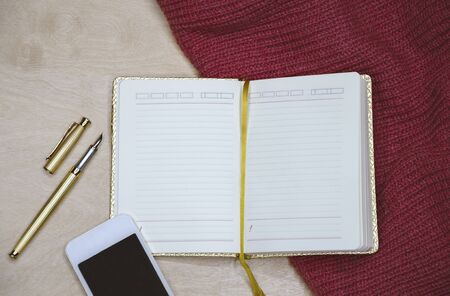 golden diary for entries with pen pen and white phone, macro photo from the top on a light...