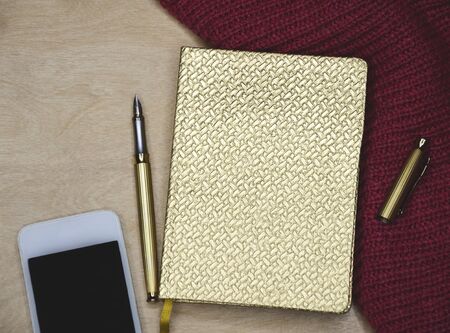 golden diary for entries with pen pen and white phone, macro photo from the top on a light...