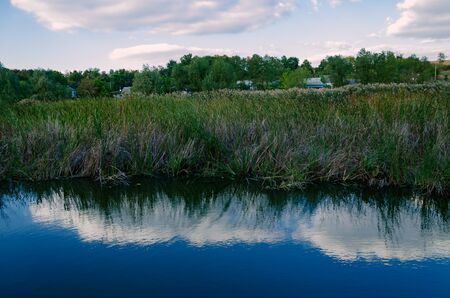 reflection of the sky with clouds in a pond on the lake with lush grass
