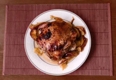 baked turkey thigh in apples on a large ceramic dish on a wooden table, close-up