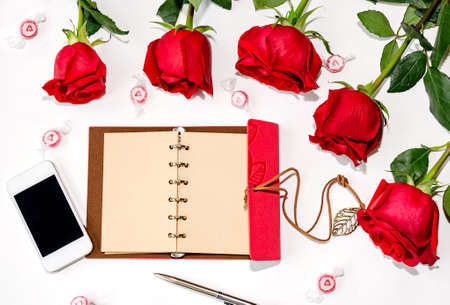 notebook with pen and phone, with red roses on a white background