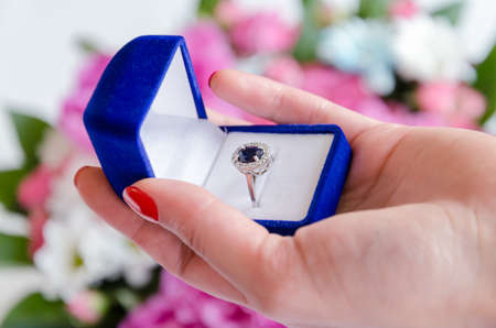 ring with a blue stone in a box in a female hand, against a background of pink flowers, a gift for...
