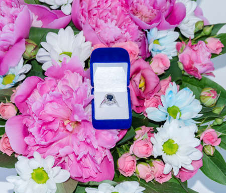 ring with a blue stone in a box, on a bouquet of pink flowers, a gift for the holiday, close-up