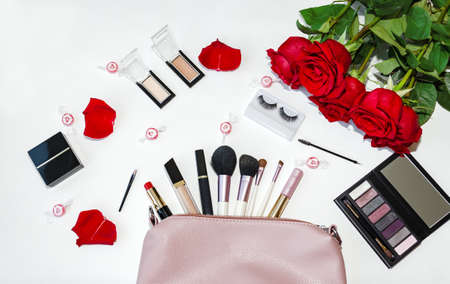 top view of working space with bag and cosmetic brushes, color cosmetics and red roses flowers