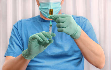 Doctor's hands in blue gloves holds a syringe and a vial of vaccine or medicine