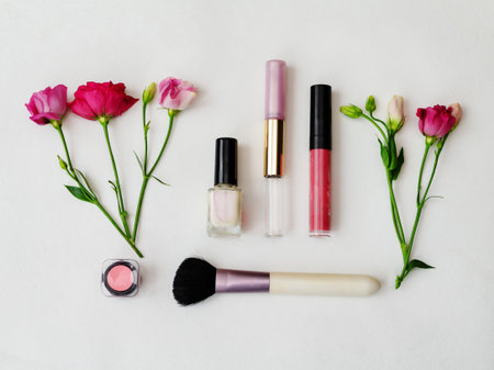 A variety of cosmetics, including lip gloss, nail polish and blush, are expertly arranged with delicate flowers. The arrangement highlights a fresh and vibrant theme for makeup lovers.の写真素材
