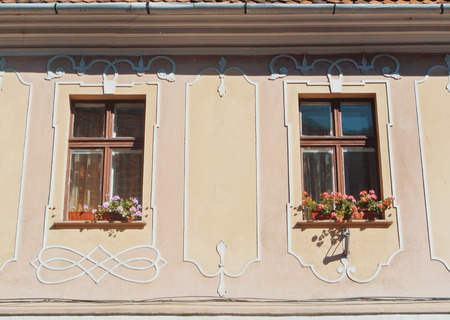BRASOV, ROMANIA - AUGUST 1, 2017: Windows of old traditional decorated pink beige romanian house with colorful flowers on sunny day.のeditorial素材