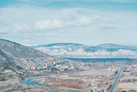 A panoramic view to caucasian mountains covered with the snow, a small village near the river and a...