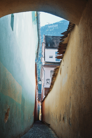 A narrow lane Strada sforii, one of the most narrow in Europe, ald vintage walls and a view to a mountain with a sign of Brasov over the town.の写真素材