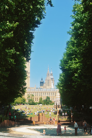 LONDON, ENGLAND - AUGUST 01, 2013: A playground and a green grass meadow with plenty of people spending time sitting eating in english park with Westminster palace and Big Ben at the background.のeditorial素材